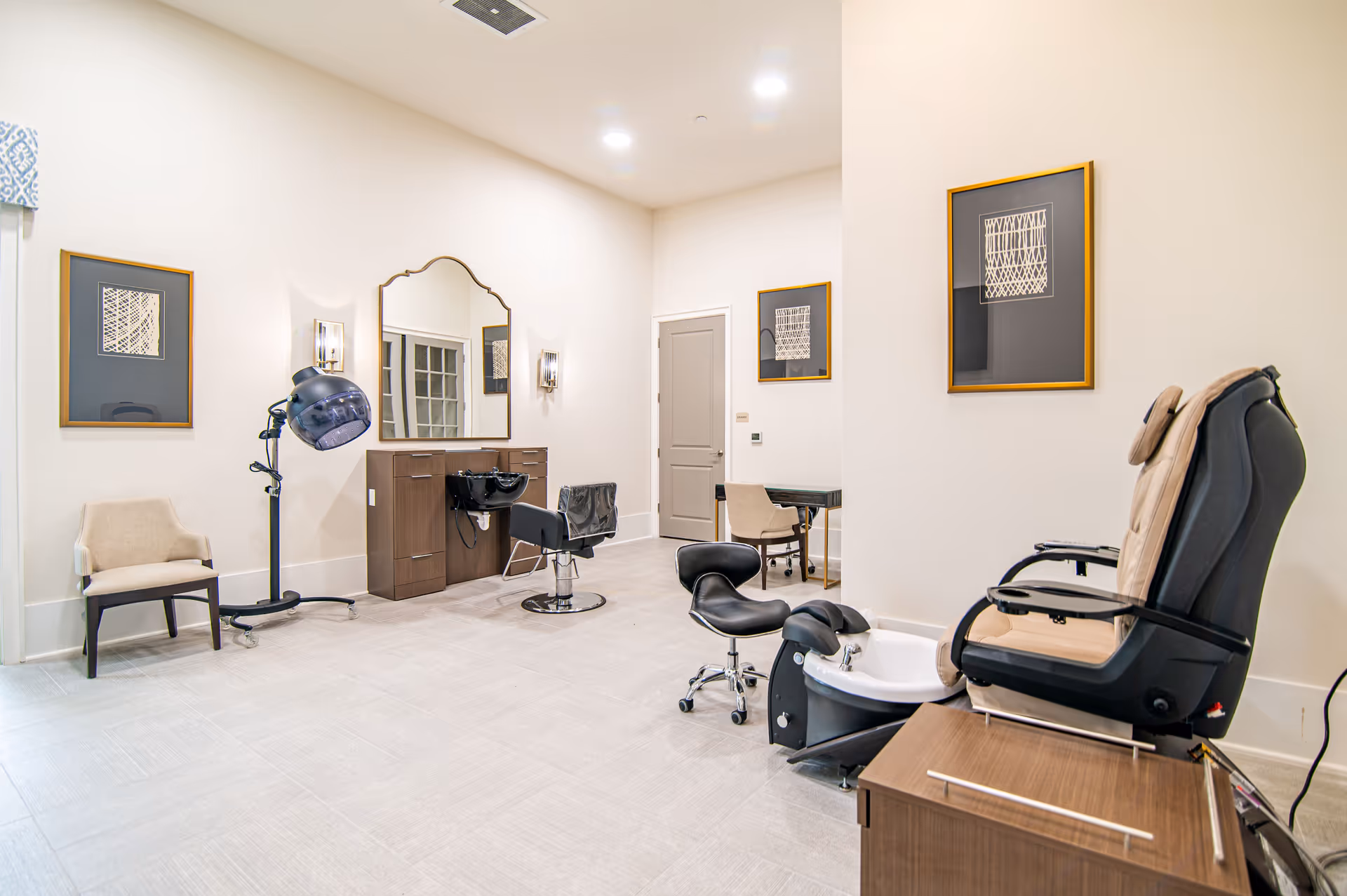 Bright salon-style room with a styling station and mirror, hooded hair dryer, pedicure chair, and additional seating.