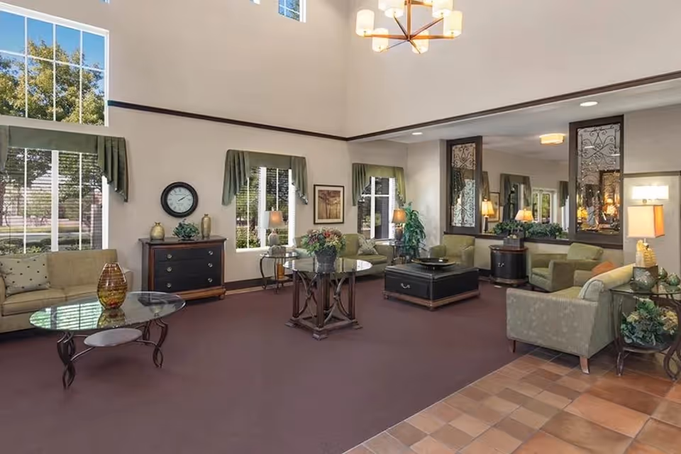 Spacious senior living facility lounge with multiple seating areas, coffee tables, large windows and high ceilings.