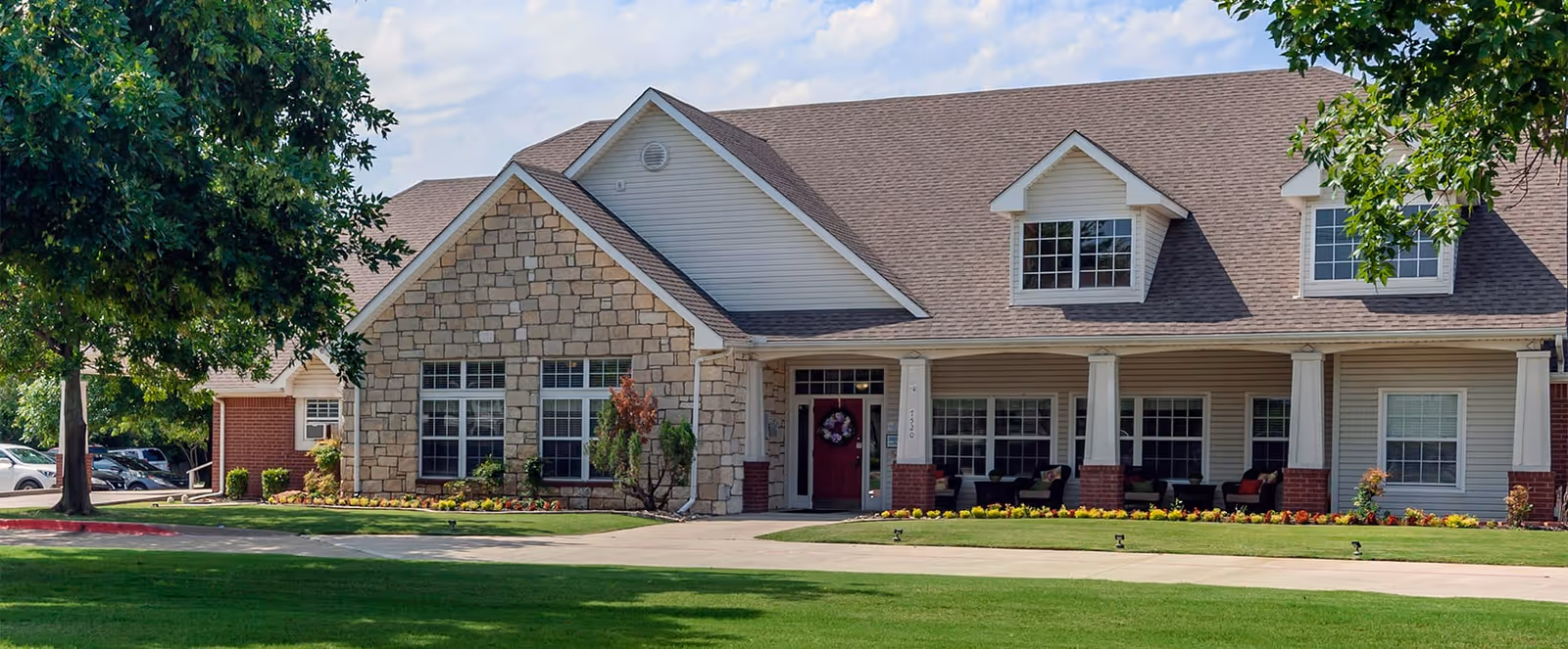 Front exterior of a single-story residential-style building with a covered porch, stone facade, dormer windows, and a manicured lawn.
