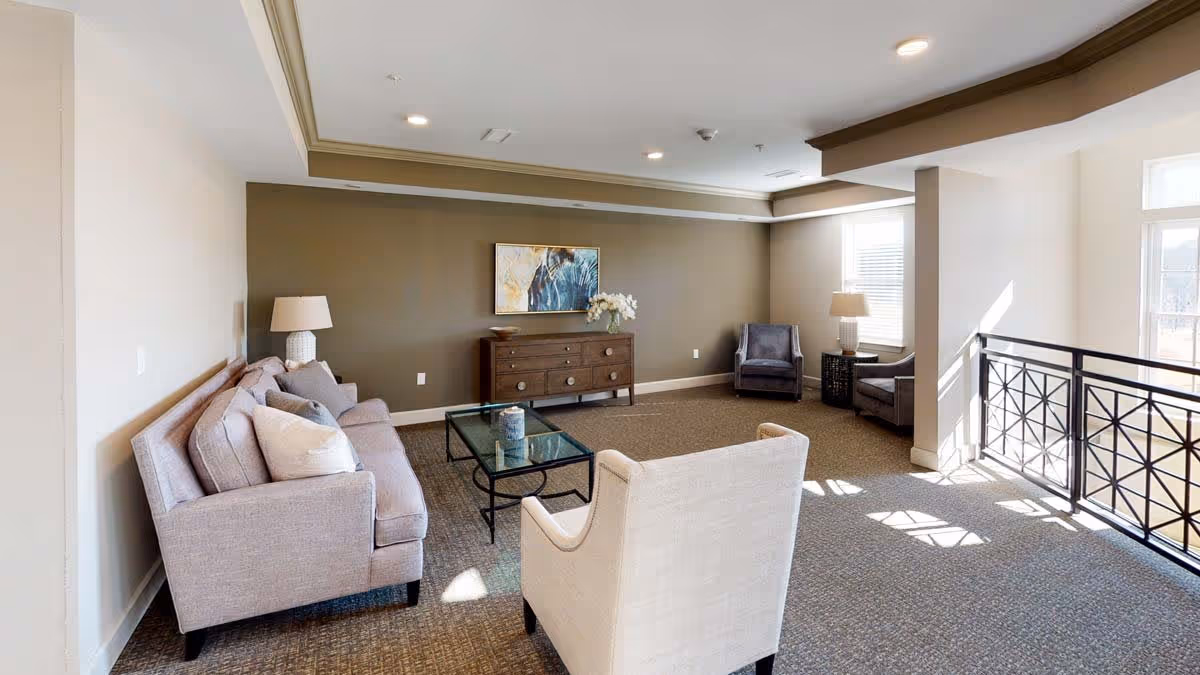 Furnished common lounge with sofas, armchairs, a glass coffee table and a sideboard against a brown accent wall.