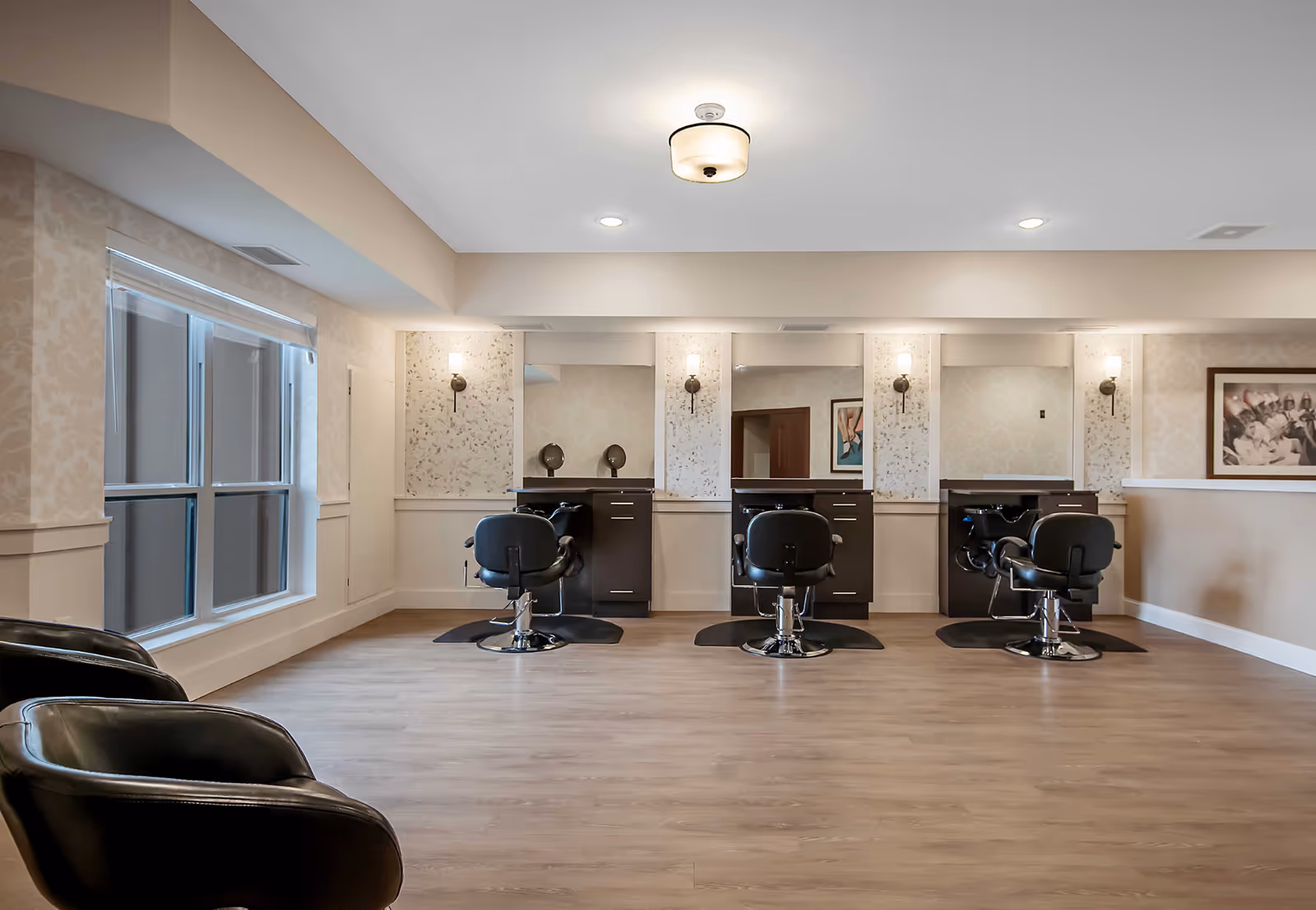 A bright salon area with three styling stations, black salon chairs, mirrors, and large windows.