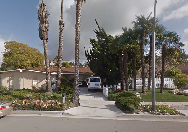 Front view of a senior living facility with palm trees, a driveway, and a white van.