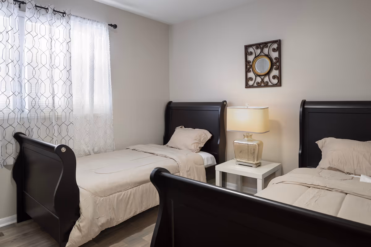 Two twin beds with dark wooden sleigh frames, a nightstand with a lamp between them and a window with patterned curtains.