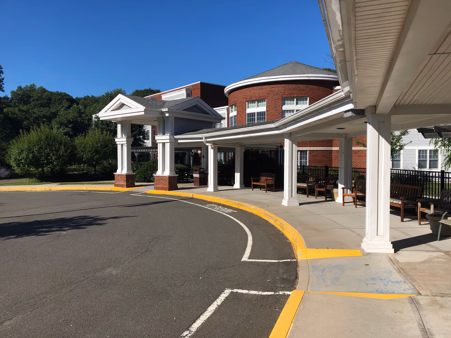 Covered porte-cochère and entrance of a brick health and rehabilitation building with benches and a circular driveway.