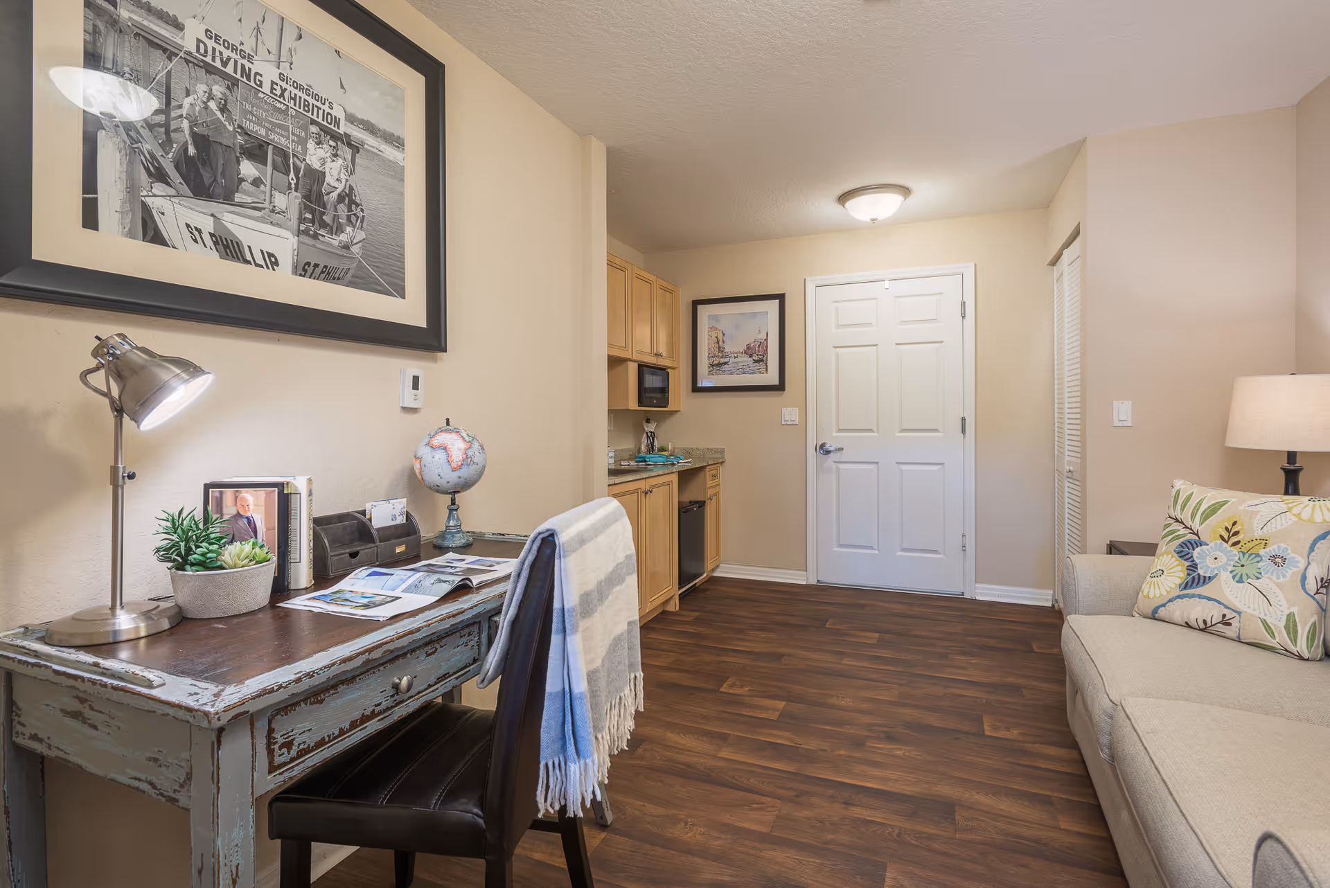 Interior living area with a rustic desk and chair, a sofa, and a small kitchenette near the entrance.
