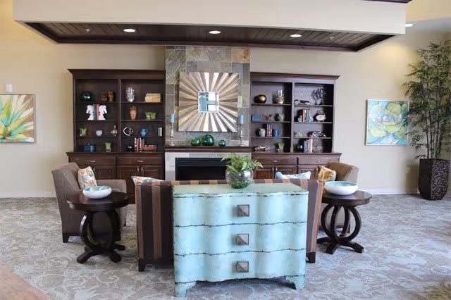 Communal living room with a fireplace flanked by built-in bookcases, seating, decorative artwork, and a turquoise chest.