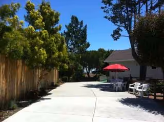 Outdoor patio area with white plastic chairs, a red umbrella, and a concrete walkway.