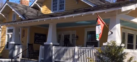 Yellow front porch of Olive Branch Family Care Homes of Union County with a flag.