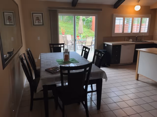 Dining area with a rectangular table and six chairs next to a kitchen and sliding glass door opening to a patio.