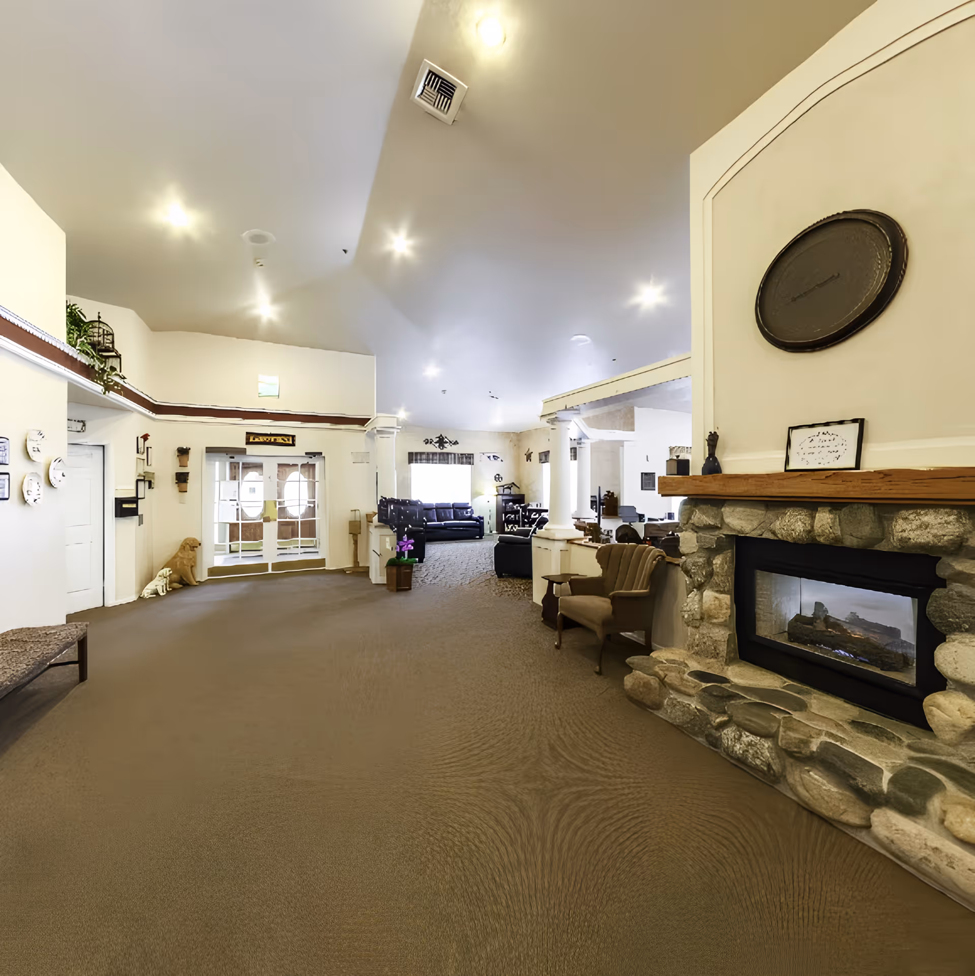 Spacious senior living facility common area with a stone fireplace, seating, and double entry doors.
