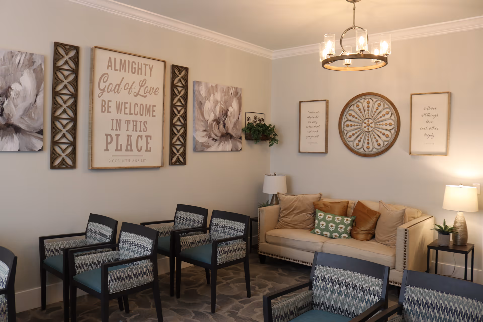 A cozy lounge with a beige sofa, patterned chairs, decorative wall art and soft overhead lighting.