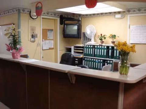 Reception area featuring a curved front desk, potted plants, and a wall-mounted TV.
