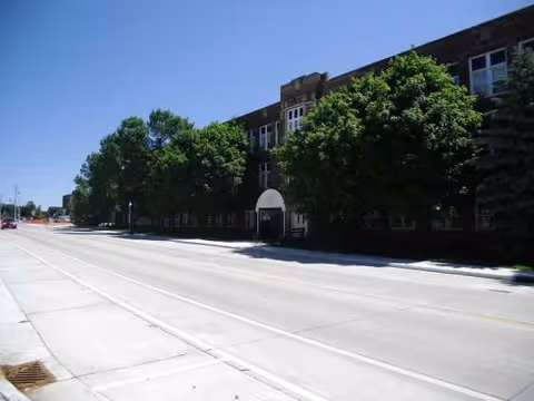 Exterior view of a brick assisted living building along a tree-lined street.