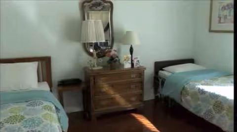 Two twin beds flank a wooden dresser with lamps in a bright, neatly arranged bedroom.