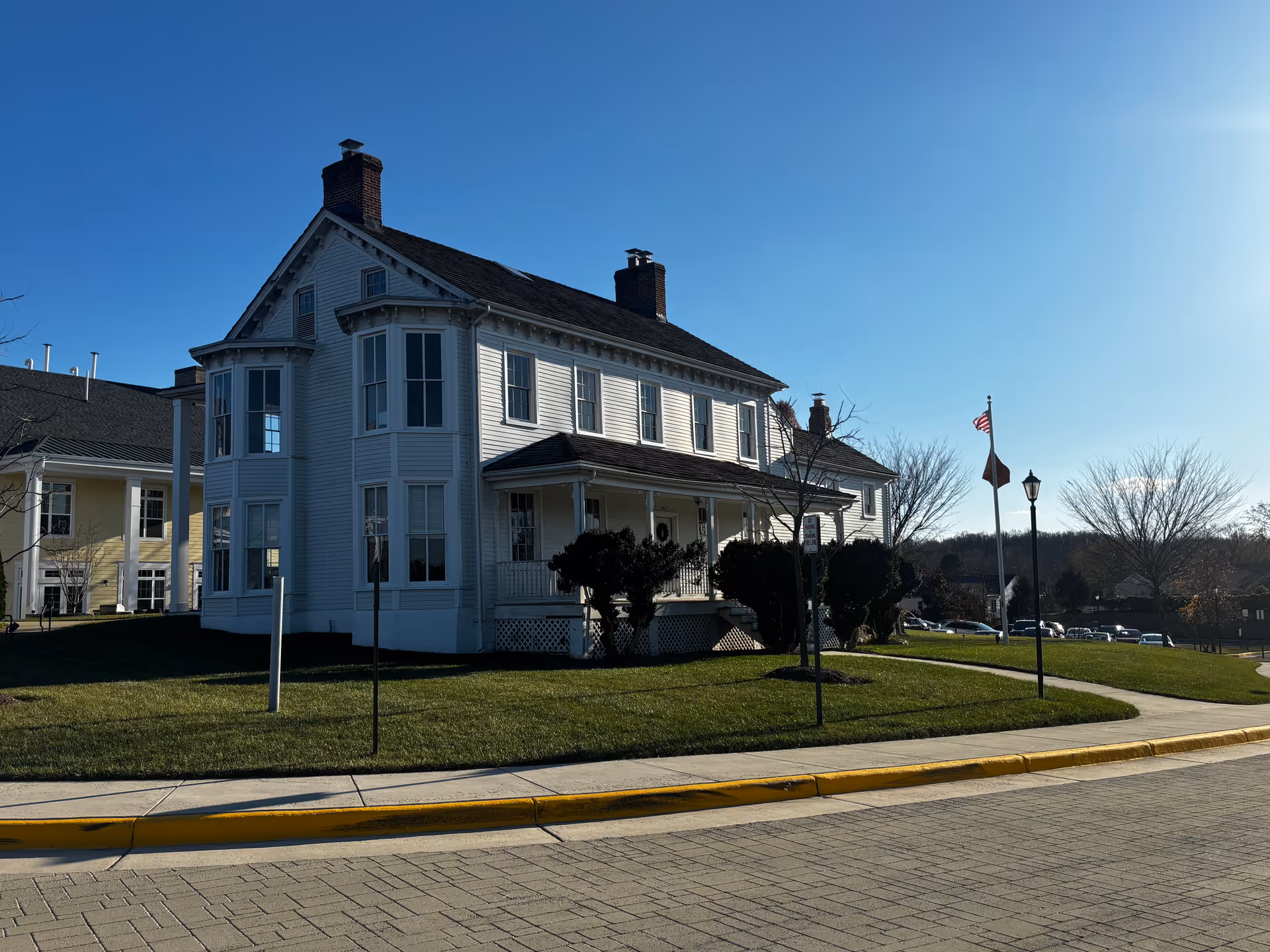 White two-story house with a front porch and bay windows on a sunny day, set on a manicured lawn with a flagpole.
