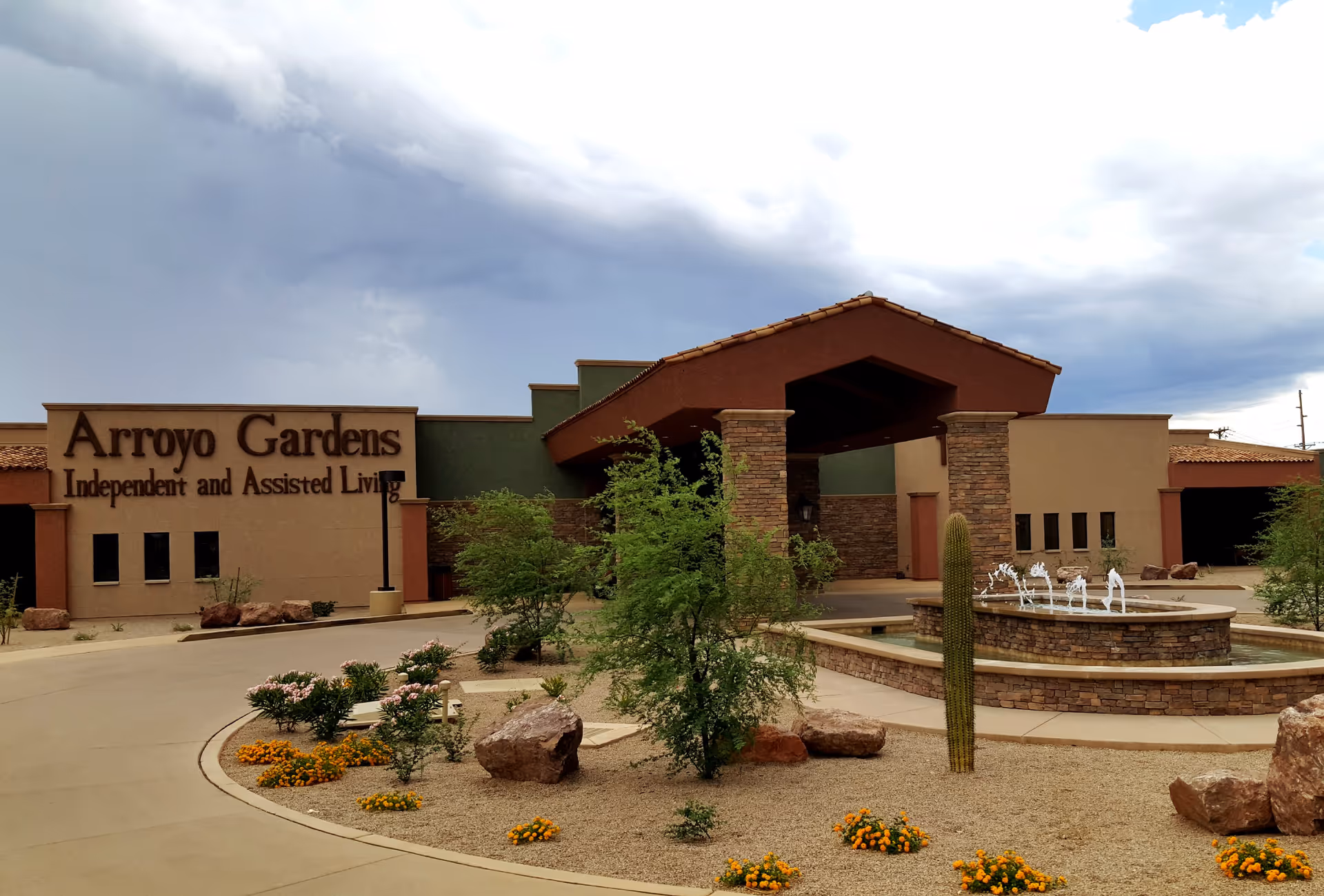 Front entrance of Arroyo Gardens independent and assisted living facility with a covered porte-cochère, fountain, driveway and desert landscaping.