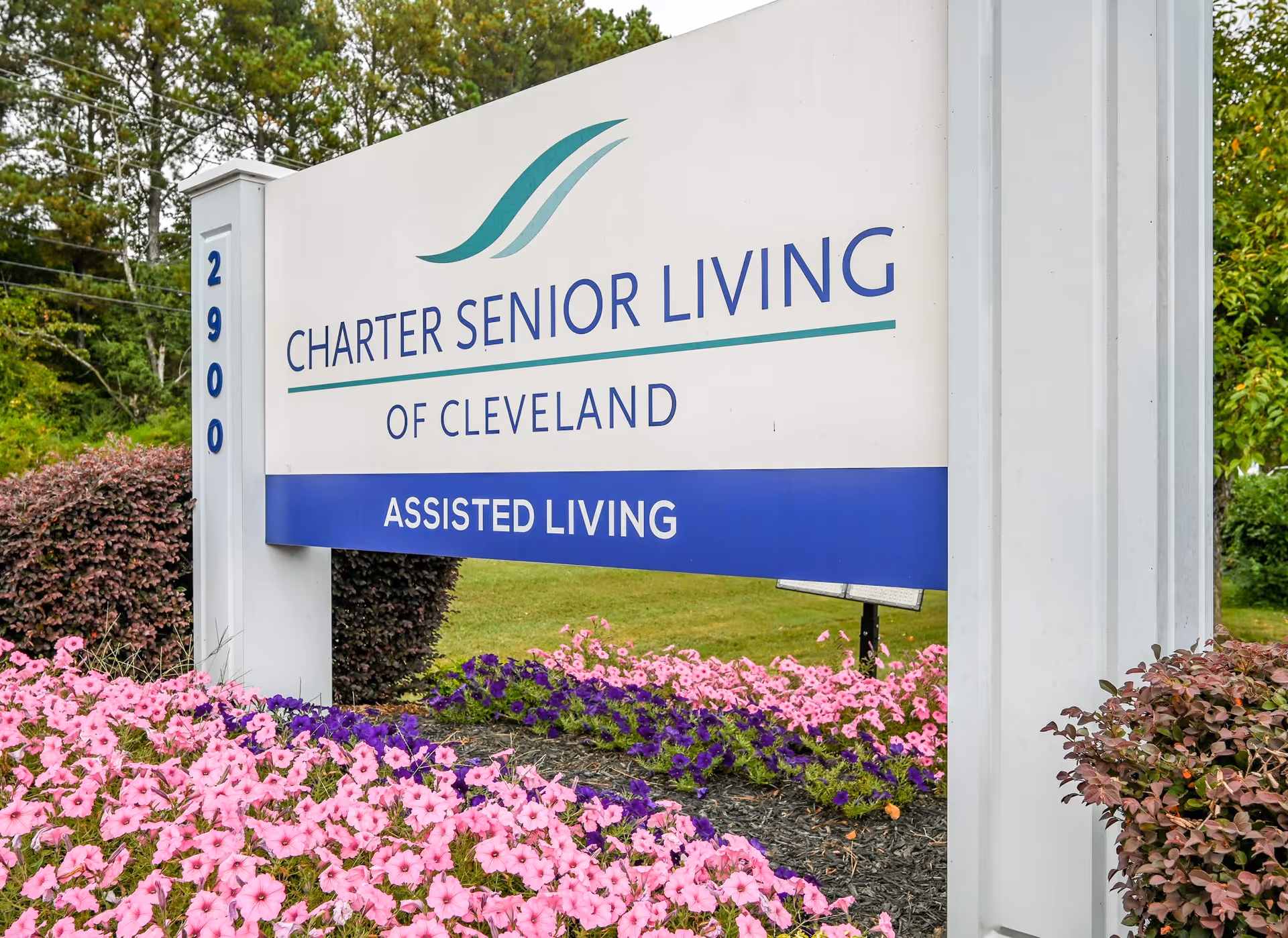 Outdoor sign for Charter Senior Living of Cleveland assisted living facility surrounded by pink and purple flowers and greenery.