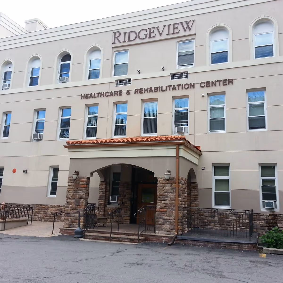 Exterior front view of Ridgeview Healthcare & Rehabilitation Center, a multi-story building with beige walls, multiple windows, and a covered entrance with stone pillars and a tiled roof.
