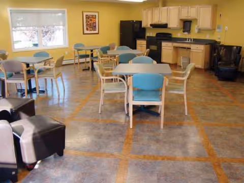 A bright dining area with multiple tables and teal chairs in a shared senior living space.