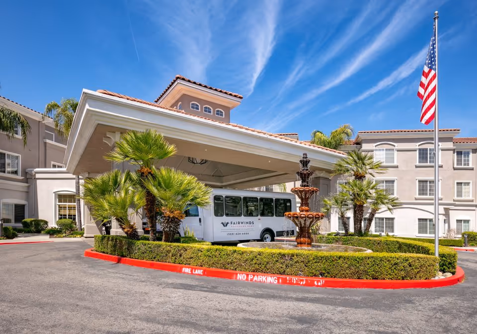 Entrance of Fairwinds - Woodward Park senior living facility featuring a fountain and a shuttle bus.