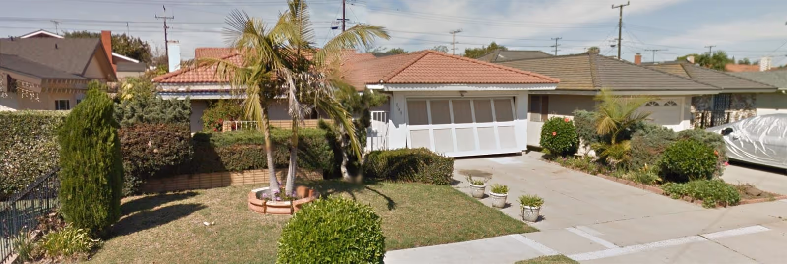 Residential-style senior living facility exterior with a driveway, palm tree, and landscaped yard