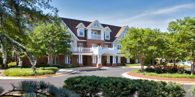 Front exterior of a brick-and-siding senior living building with a covered entrance, balconies, and landscaped driveway.