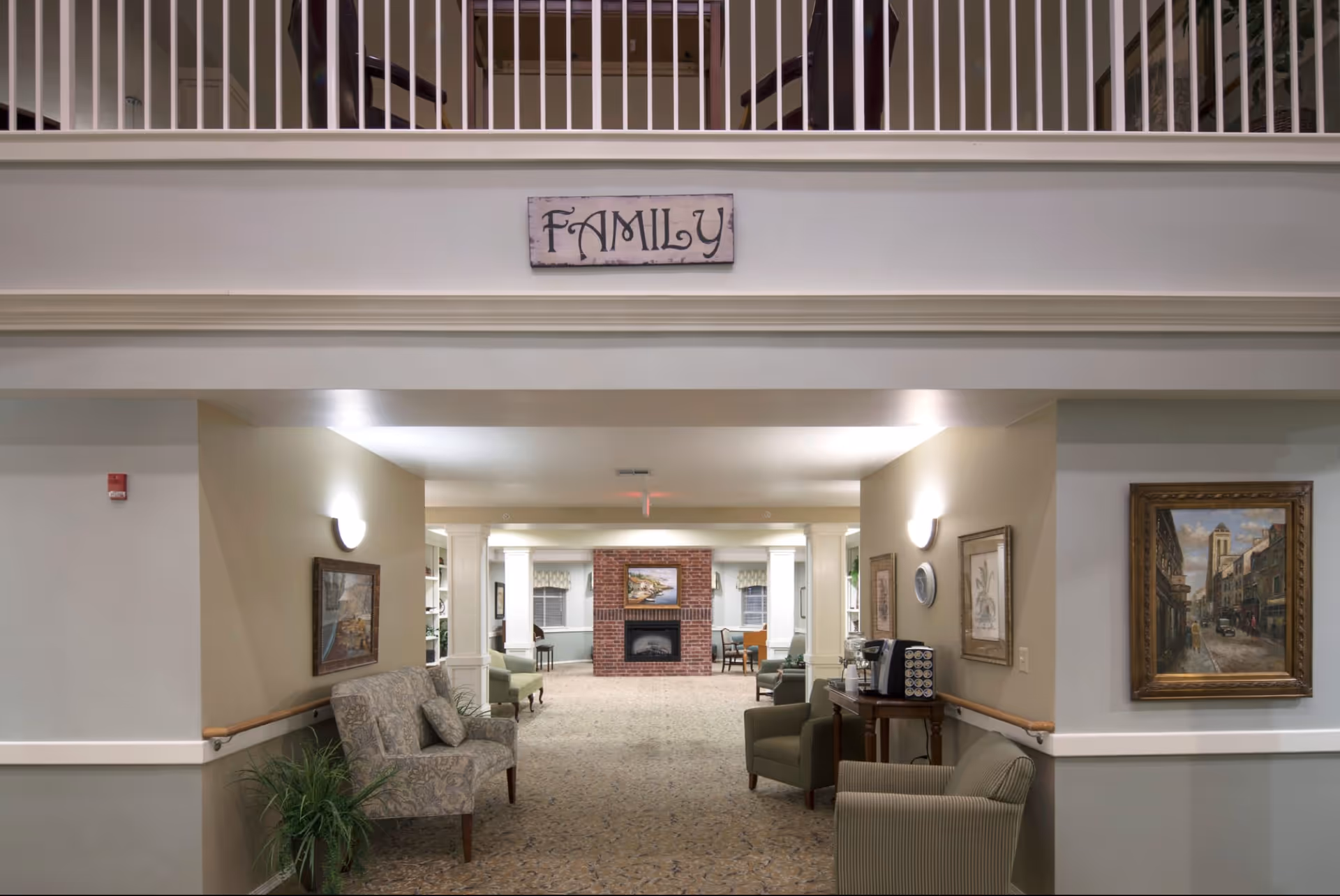 Spacious assisted living common area with chairs and tables, a fireplace at the far end, and a 'FAMILY' sign above an open balcony.