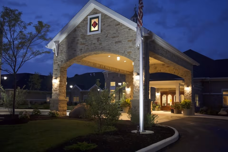 Illuminated stone porte-cochere and main entrance of a senior living building at dusk.