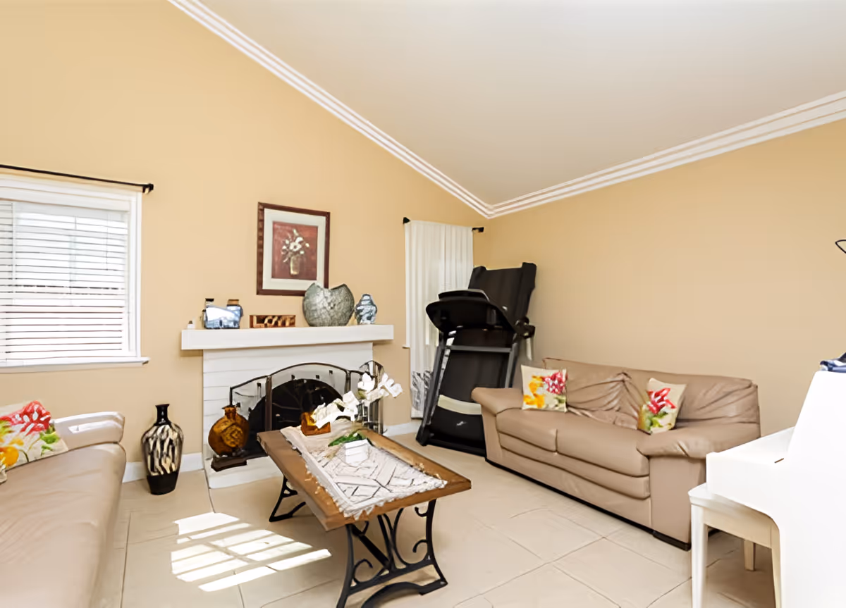 Bright living room with beige sofas, a coffee table, a fireplace, and a treadmill under a vaulted ceiling.