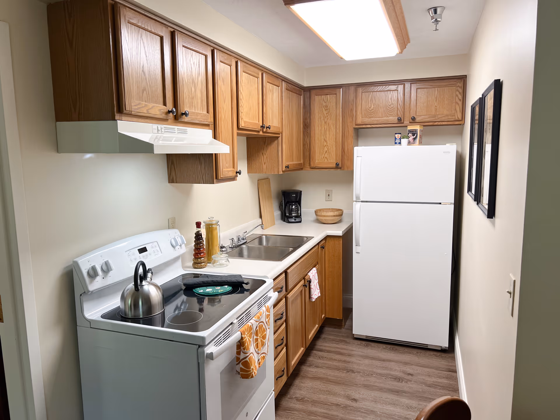 Narrow galley kitchen with oak cabinets, a white stove and refrigerator, sink, and small appliances on the countertop.