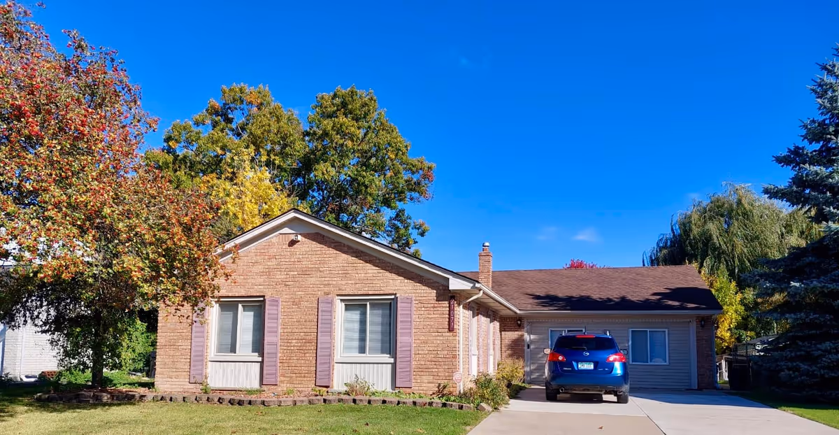 Brick, single-family home with a driveway, blue SUV, and autumn trees.