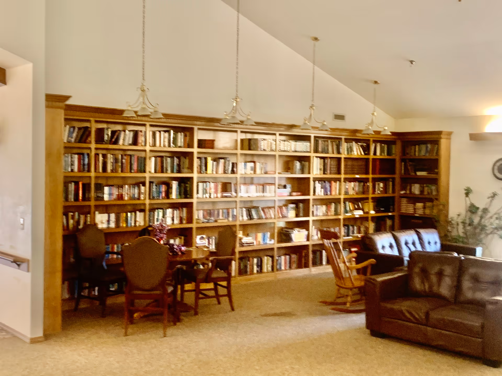 A warm communal library-style lounge with floor-to-ceiling bookshelves, several chairs and tables, and leather sofas.