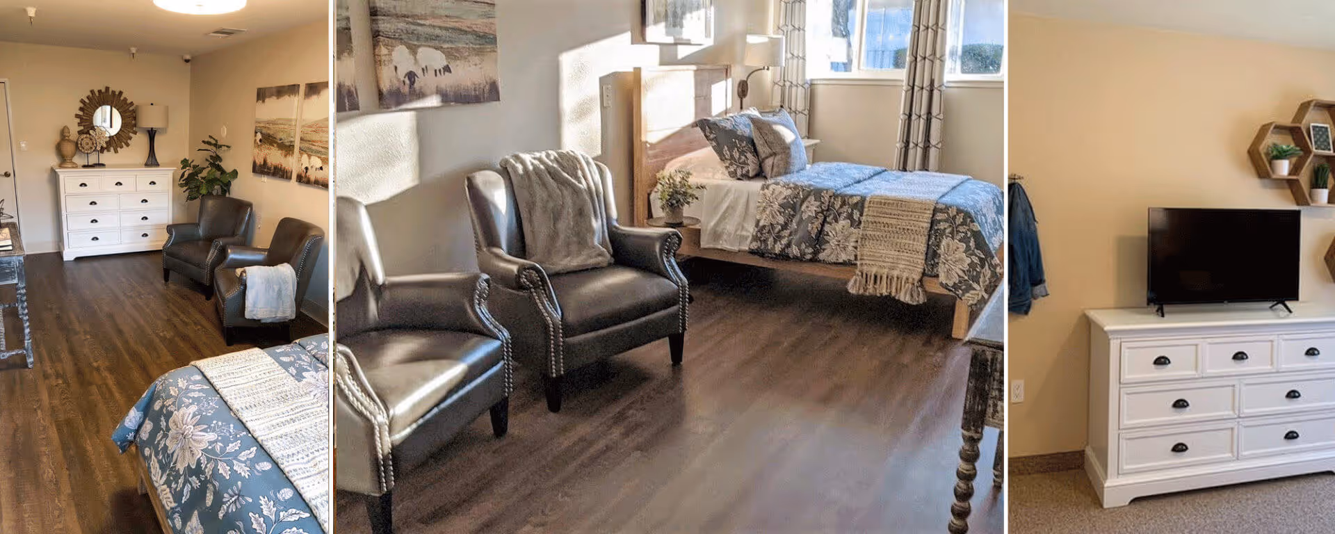 A cozy bedroom in a senior living facility featuring a bed with floral bedding, two dark leather armchairs with a throw blanket, a white dresser with decorative items and a mirror above it, a TV on a white cabinet, and hexagonal wall shelves with small plants. The room has wooden flooring and large windows with patterned curtains letting in natural light.