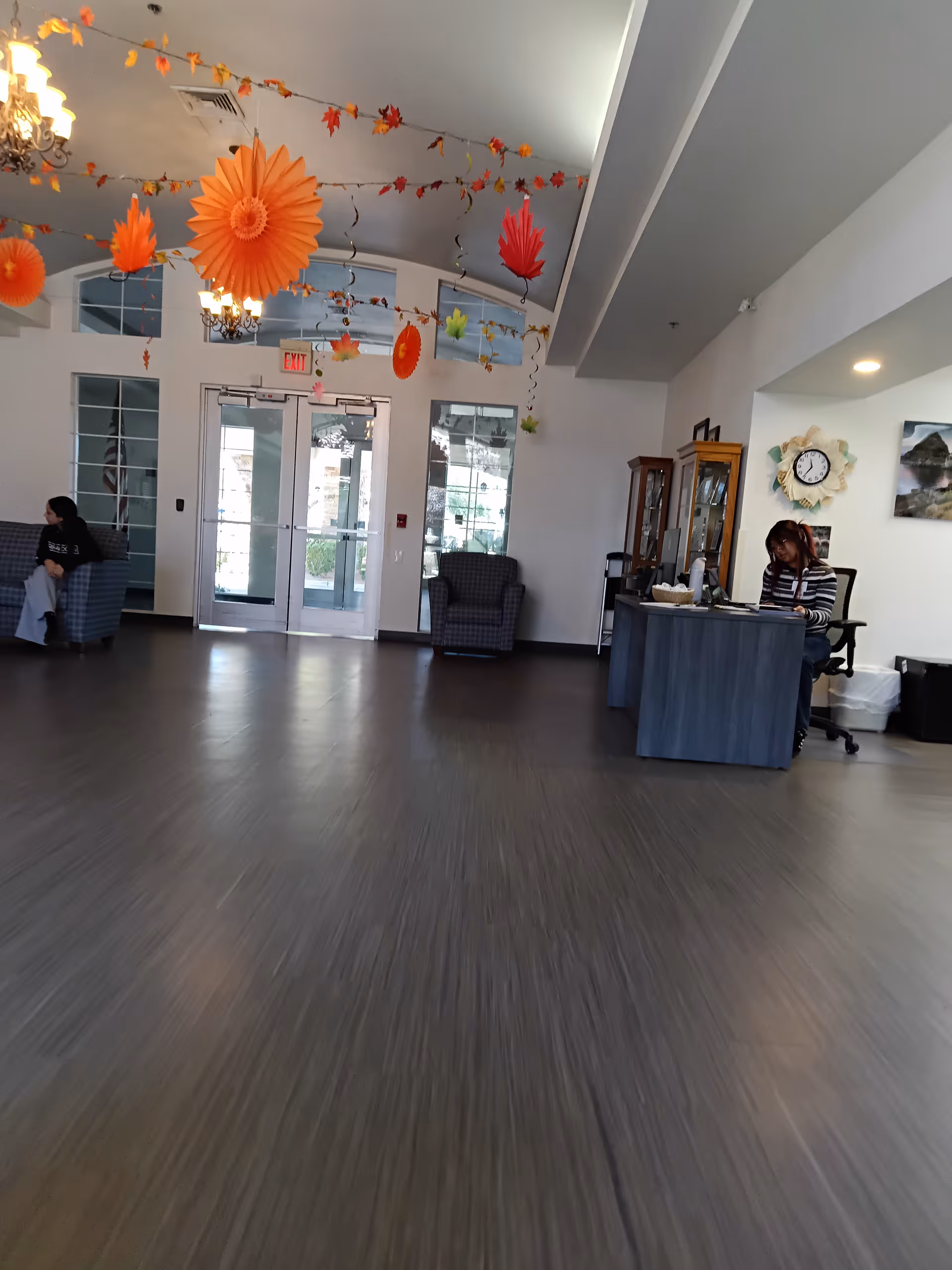 Spacious senior living lobby with a reception desk, seating, and orange hanging decorations.