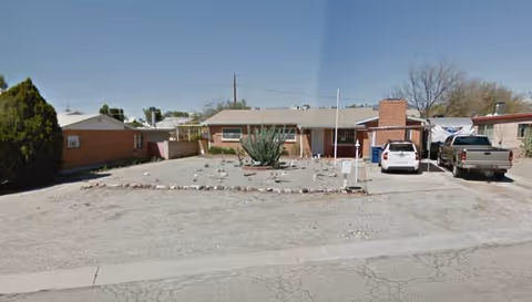 Single-story building with a gravel front yard, cactus, and parked cars.