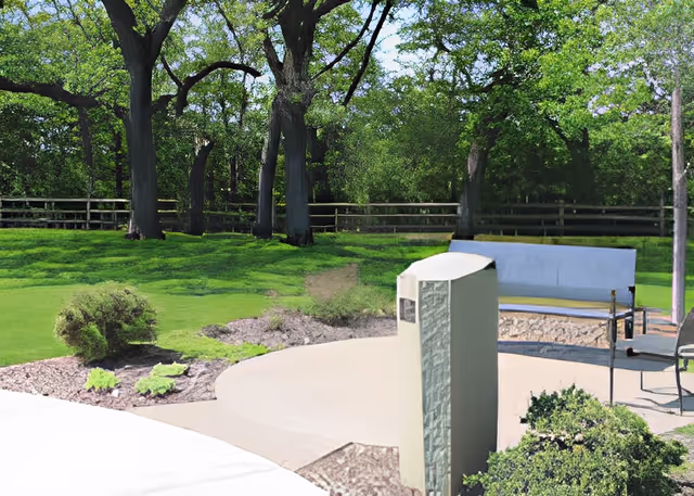 Outdoor patio with a bench and paved seating area overlooking a grassy lawn, trees, and a wooden fence.