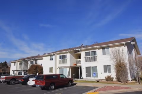 Exterior view of a two-story senior living building with several parked vehicles in front.