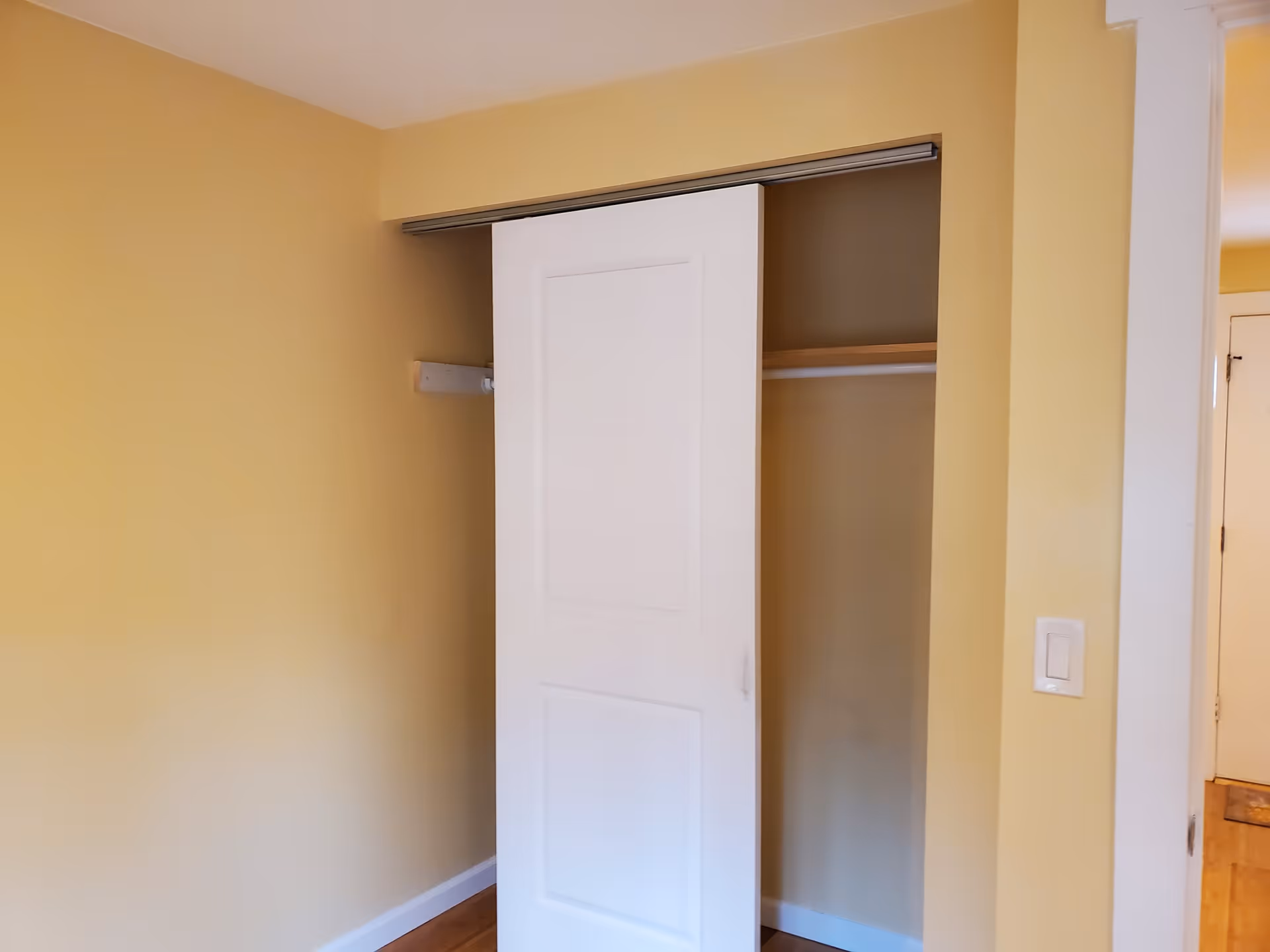 Partially open white sliding closet door in a room with yellow walls and hardwood floor.