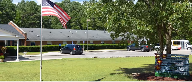 Front exterior of Hermitage Retirement Center with a flag, trees, and a parking lot.