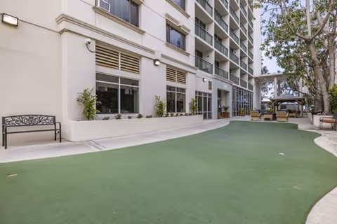 Outdoor courtyard of a multi-story residential building with green artificial turf, benches, balconies, and a shaded seating area.