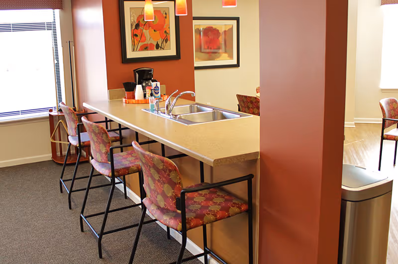 Community kitchenette with a long counter, sink and several patterned bar stools in a common area.