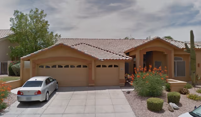Exterior view of a single-story beige assisted living building with a three-car garage and desert landscaping.