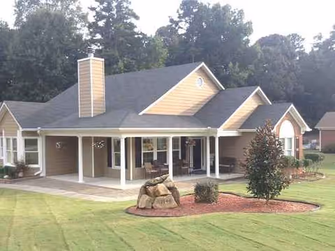 Single-story Sunshine Residential Care building with a front porch, manicured lawn, and landscaped rocks.
