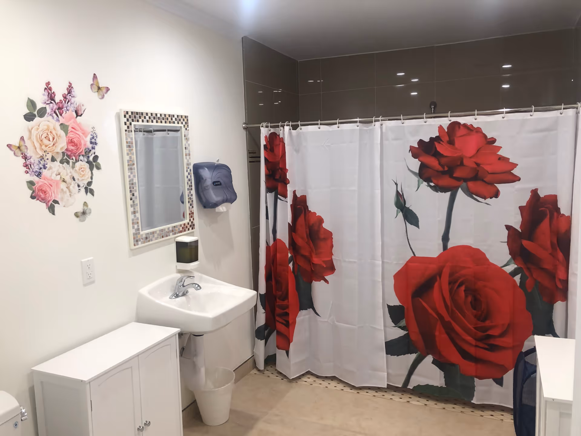 Bathroom with a sink and mirror, floral wall decal, and a shower with a large red-rose shower curtain.