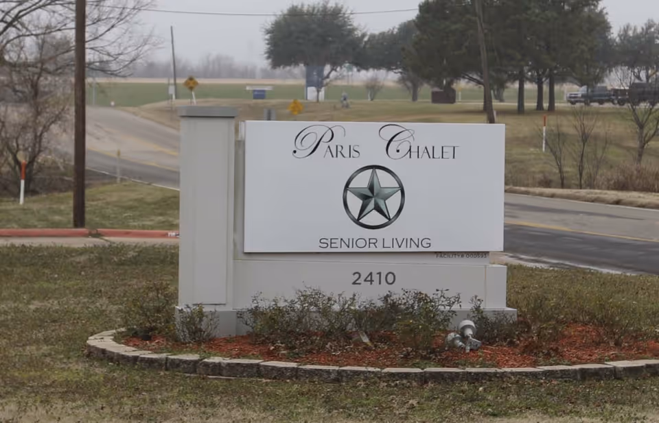 Entrance sign for Paris Chalet Senior Living with address 2410 on a landscaped roadside median.