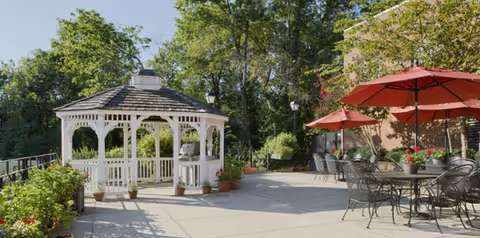 Sunny outdoor patio featuring a white gazebo and red umbrella tables.