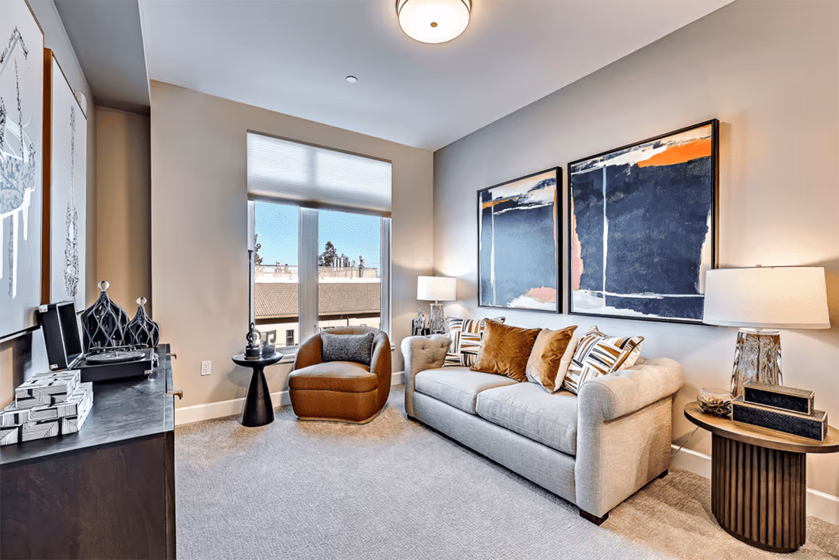 Modern living room with a light gray sofa, accent chair, large abstract paintings, lamps, and a window.