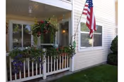 Exterior view of an apartment porch with a white railing, hanging flower baskets, and an American flag.