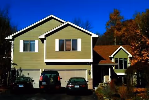 Two-story green building with a garage and several cars parked in the driveway.
