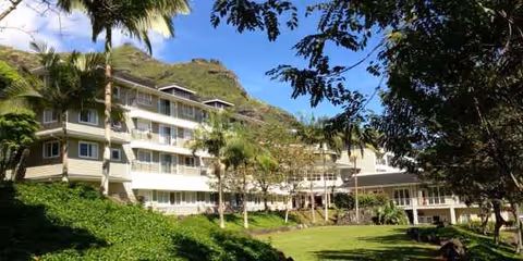 Exterior view of Oceanside Hawaii senior living building with balconies, palm trees, and lawn.